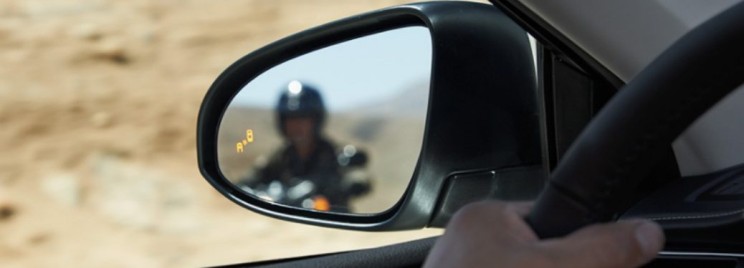 Car side mirror showing blind spot detection alert with a motorcyclist approaching